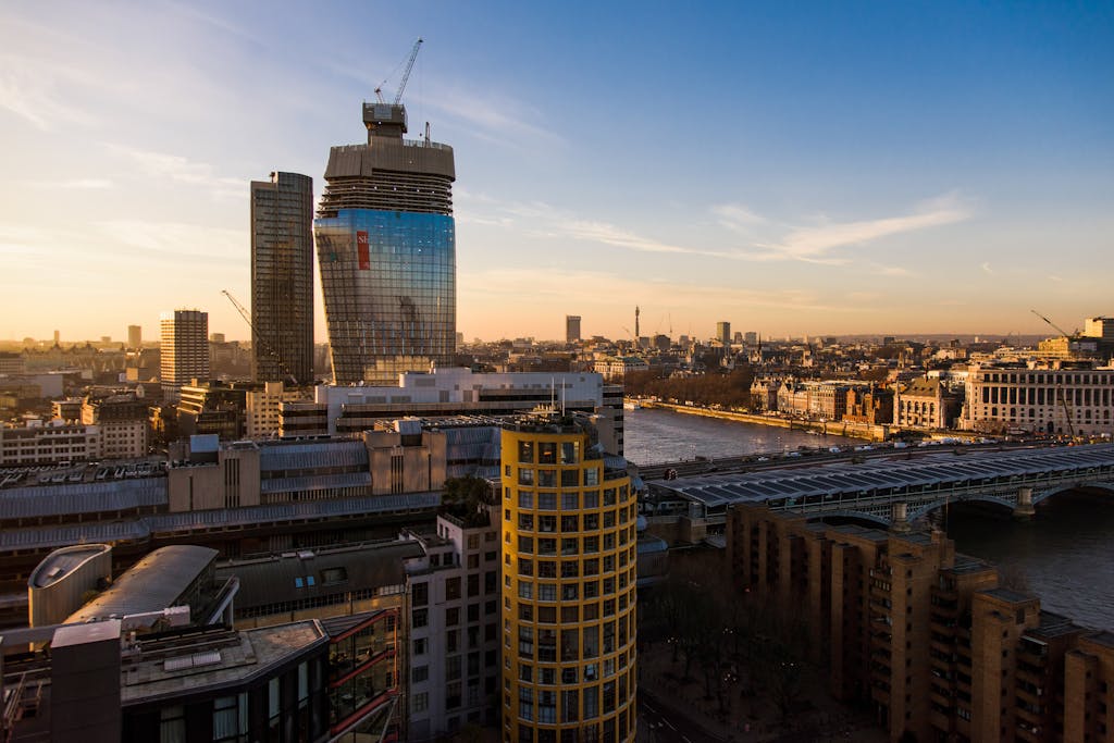 Contemporary multistory financial buildings and residential houses located on streets near calm river with bridge in London city in evening time